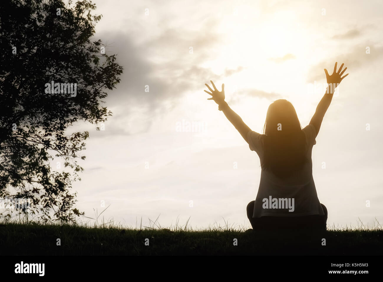 Ein glückliches asiatische Frau ist entspannend auf grünem Gras und angehoben bis zu Sky Arme auf sonnigen Sommertag mit Park Hintergrund. Konzept von Wohlbefinden und gesunde l Stockfoto