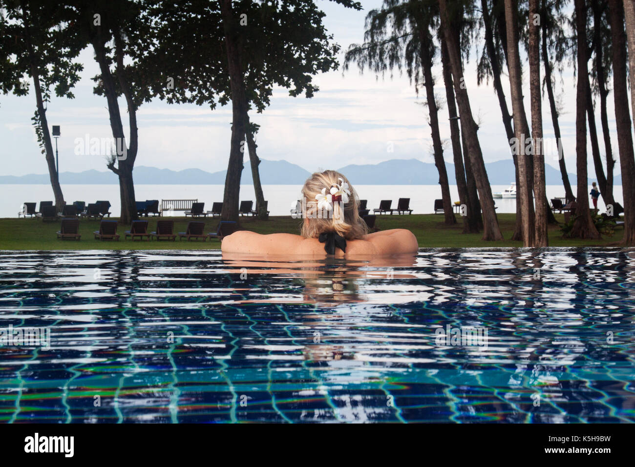 Frau im Pool in Thailand mit Blick auf das Meer. Frau entspannend in der Nähe der Strand von Krabi. Weiß plumeria Flower auf eine Frau Haar. Andaman Meer Stockfoto