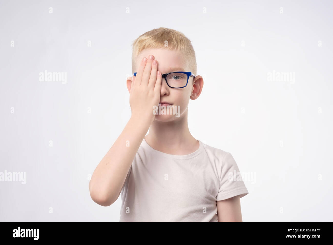 Kaukasische blonde Kind Überprüfung des Sehvermögens schließen die Hälfte der Fläche mit der Hand. Stockfoto