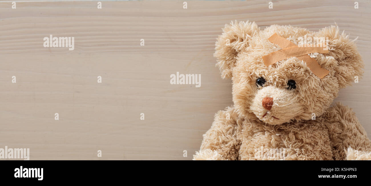 Das Kind ist krank Konzept. Teddybär mit Bandage sitzen auf einem Holzboden Stockfoto