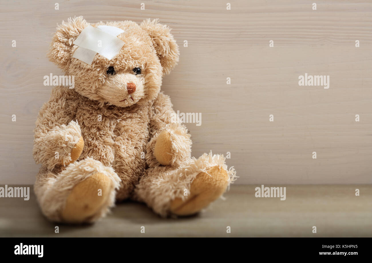 Das Kind ist krank Konzept. Teddybär mit Bandage sitzen auf einem Holzboden Stockfoto