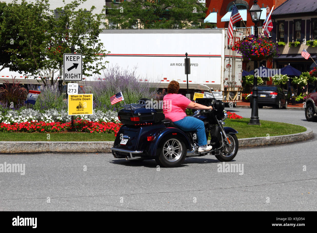Bikerin auf einem Motortrike, die während der Bike Week in Gettysburg, Adams County, Pennsylvania, USA, am Schild „Town Throttle Down“ am Lincoln Square vorbeifährt Stockfoto