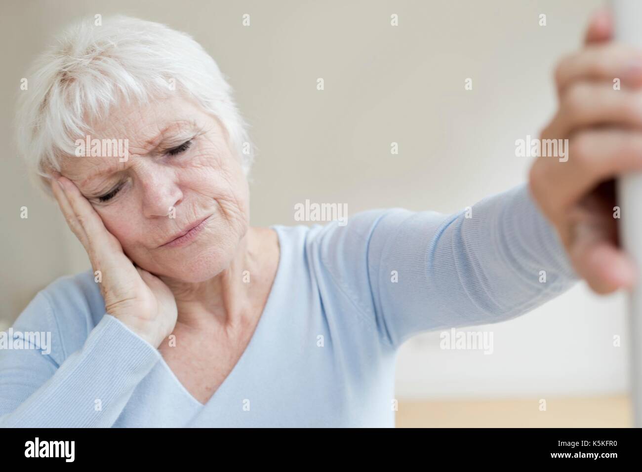Ältere Frau mit Kopfschmerzen, lehnte sich an der Wand. Stockfoto
