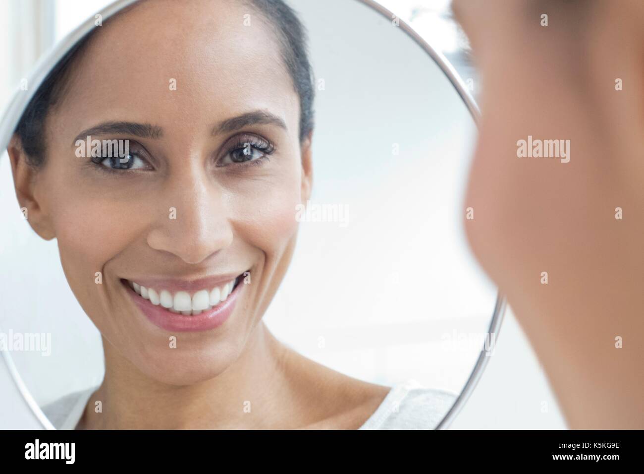 Mitte der erwachsenen Frau im Spiegel zu betrachten, ein Lächeln auf den Lippen. Stockfoto