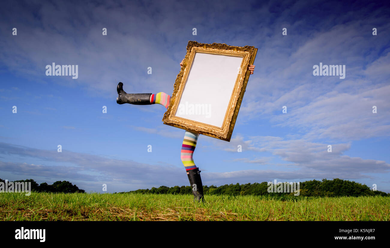 Ein schräges, schräges Beinpaar unter einem leeren goldenen Bilderrahmen, der über Felder läuft. Stockfoto