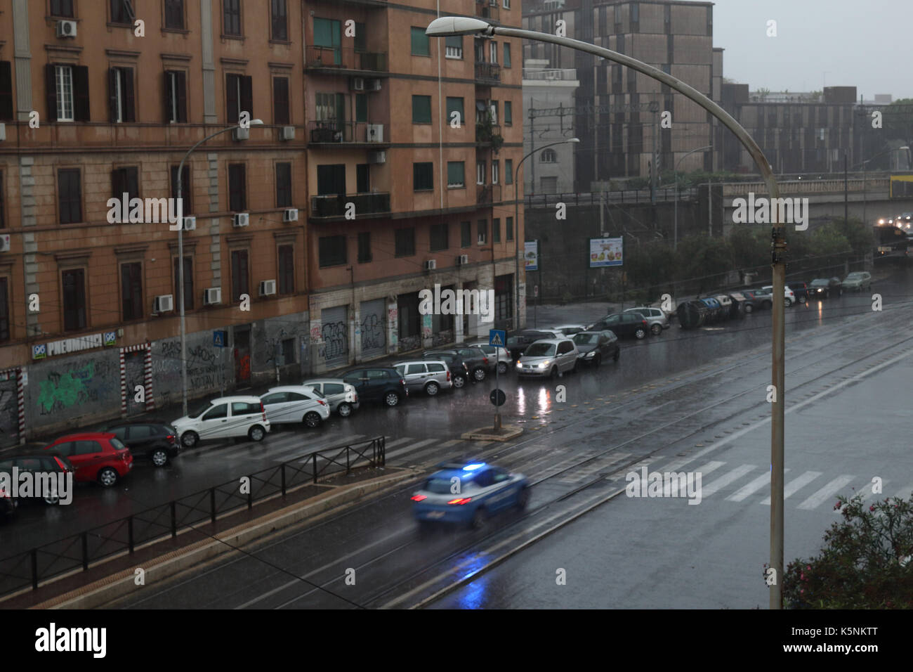 Geparkte Autos und ein Polizeiauto im Regen an der Via Prenestina. Rom, Italien. Stockfoto
