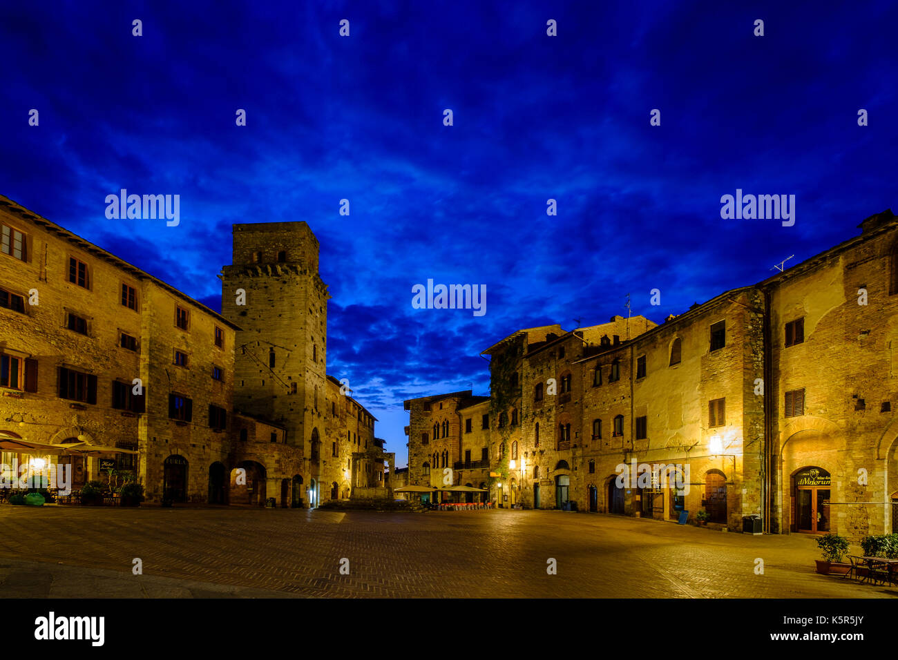 Alte Häuser umkreisen den Piazza Della Cisterna in der Mitte der mittelalterlichen Stadt, nachts beleuchtet Stockfoto