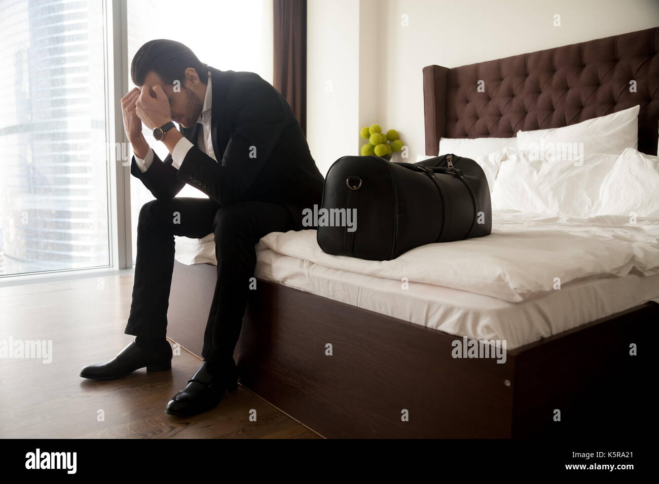 Frustrierter Mann in Anzug sitzen auf dem Bett neben Gepäck Tasche. Stockfoto