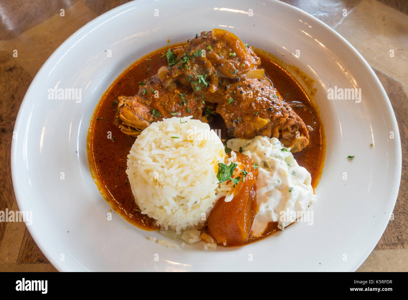 Eine Schüssel Goan Lamm curry serviert mit Kardamom Reis, Joghurt und Mango Chutney Stockfoto