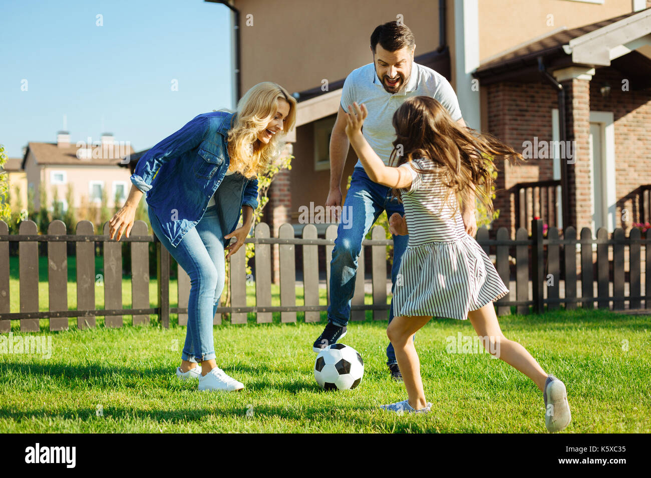 Kleine Tochter Fußball spielen mit ihren Eltern außerhalb Stockfoto