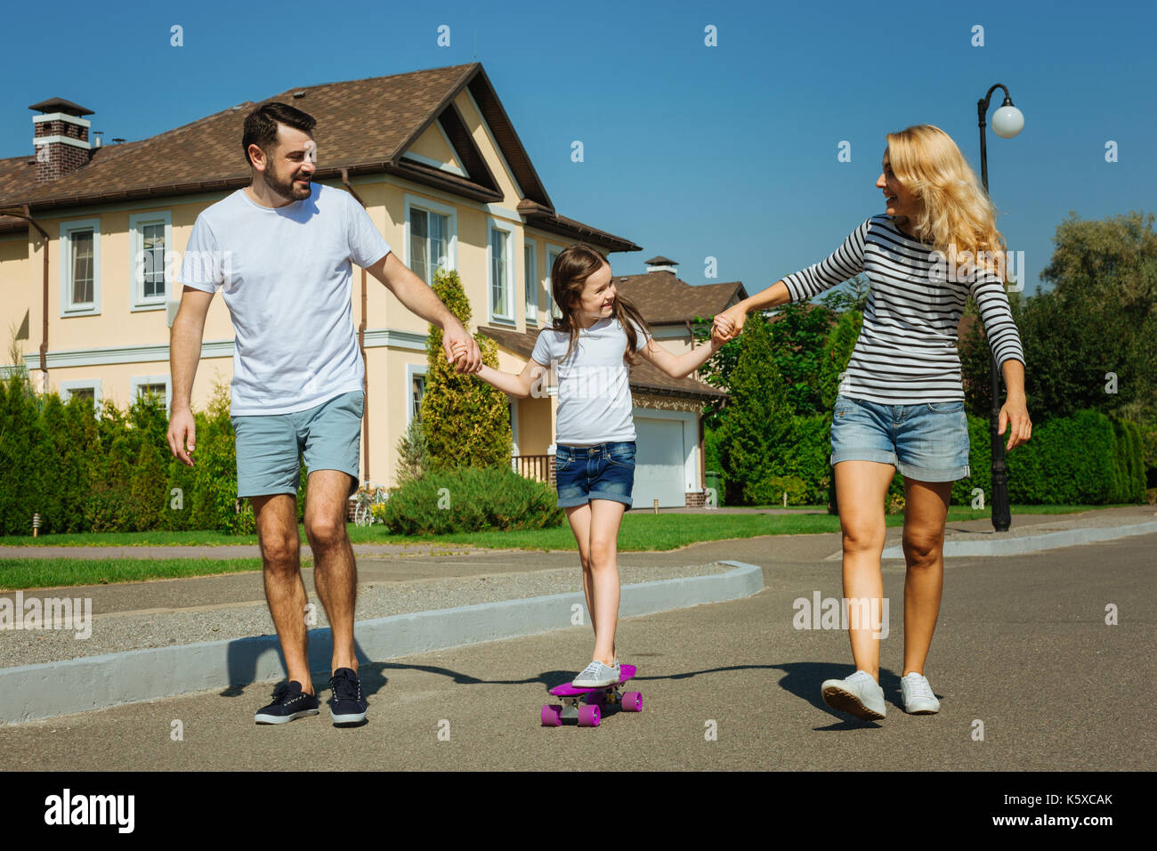 Liebevolle Eltern lehre Tochter Skateboard zu fahren Stockfoto