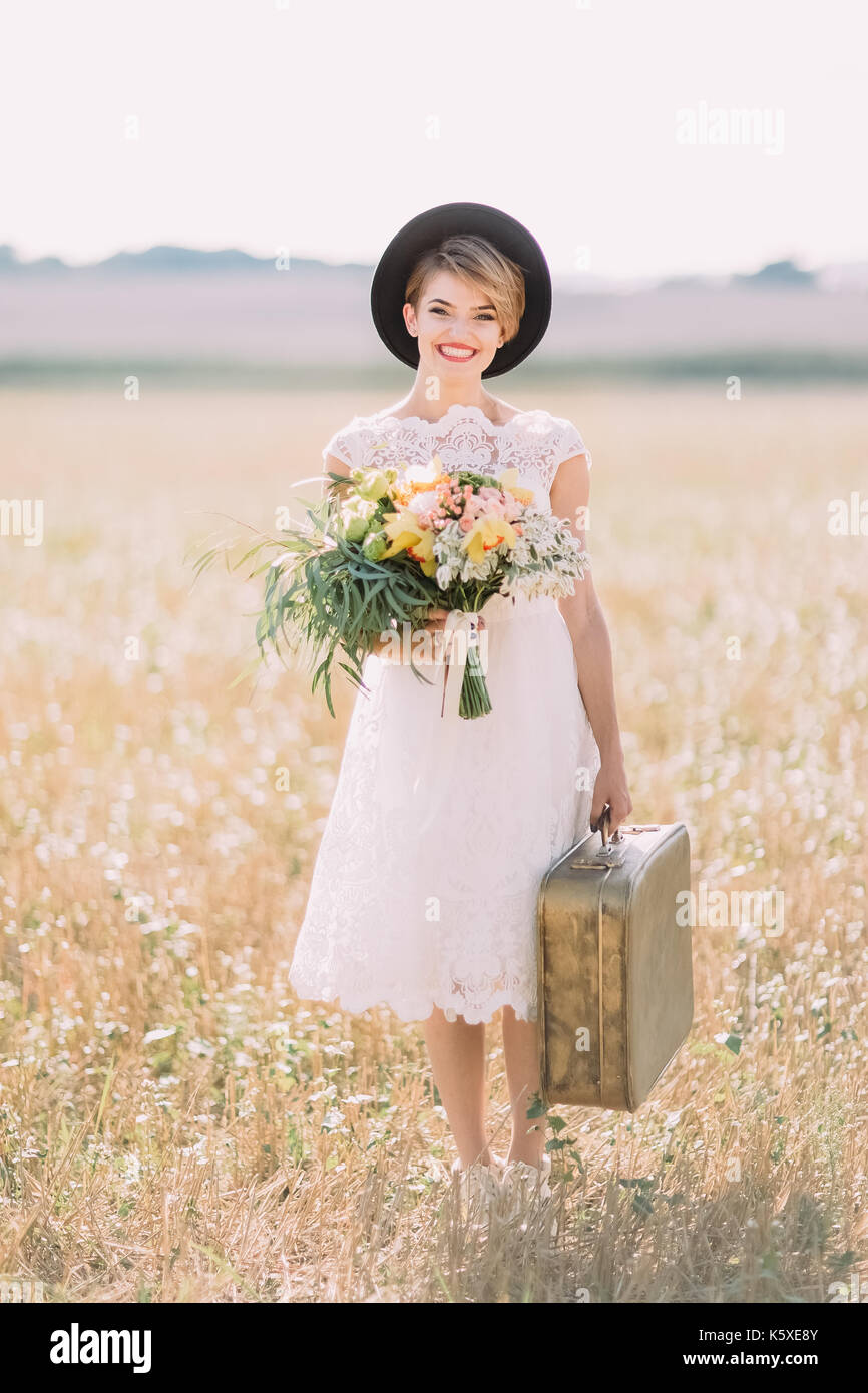 Die in voller Länge Foto der schönen Lächeln Braut im Knie - Länge Hochzeit Kleid auf dem Hintergrund der sonnigen Gebiet. Stockfoto