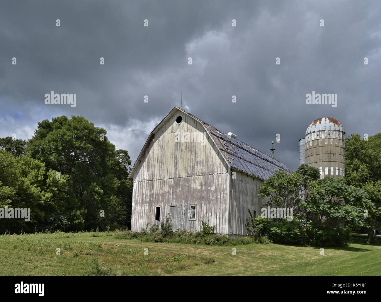 Eine große weiße, verwitterte Scheune steht mit einem Silo. Stockfoto