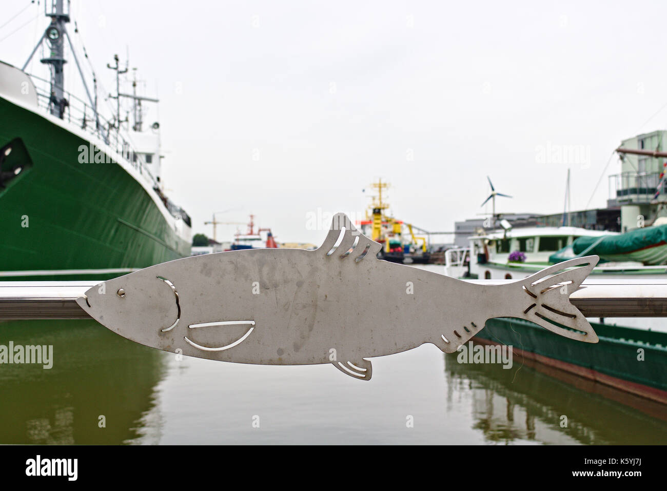 Metall Geländer mit flachen Fischen-förmige Ornament und Blick auf den Hafen im Hintergrund (von einer öffentlichen Straße erschossen, kein Privatbesitz) Stockfoto