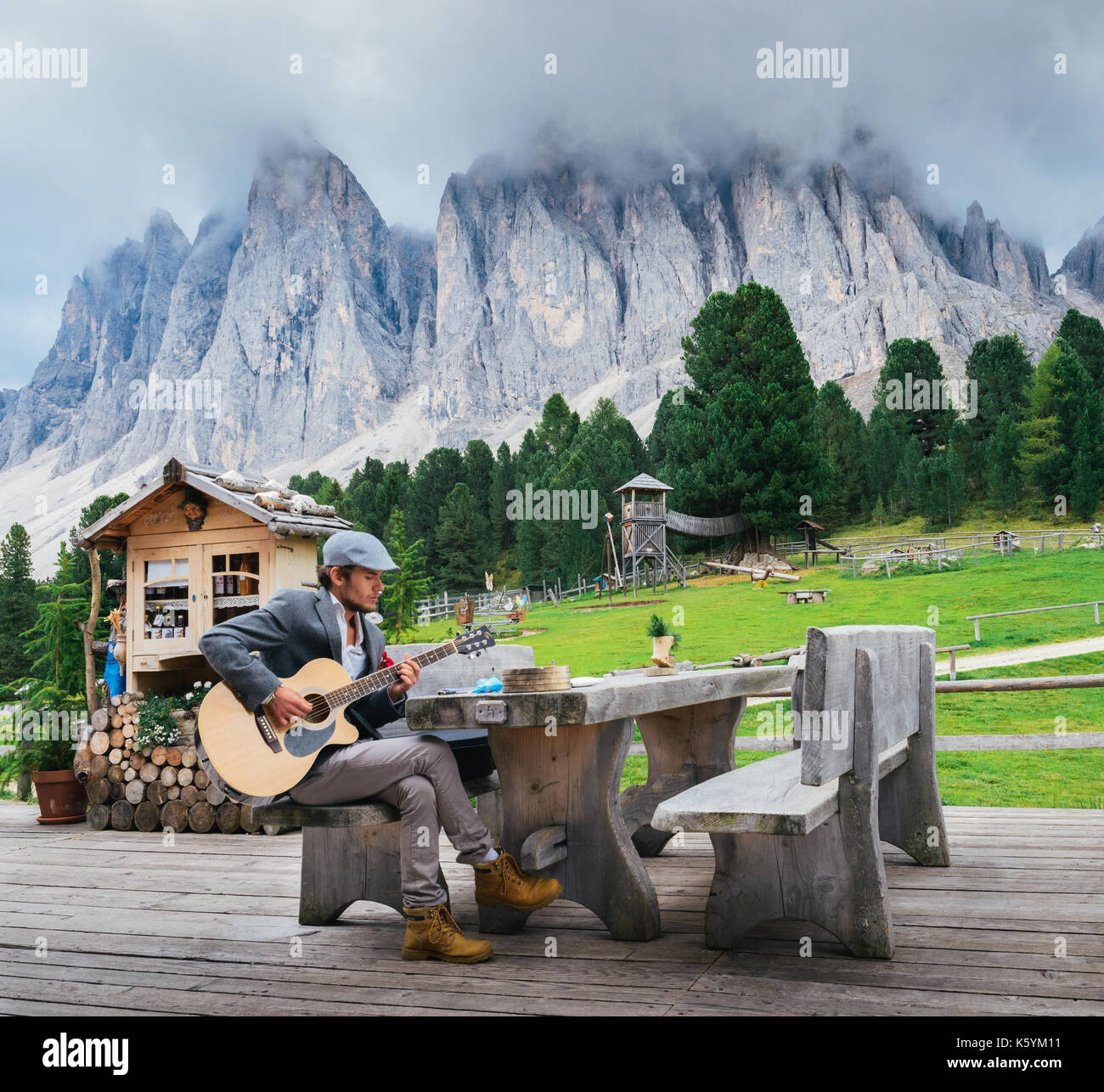 Junge gut gekleideten Mann (30-35) spielt eine Gitarre mit italienischen Dolomiten Felsformation Hintergrund Stockfoto