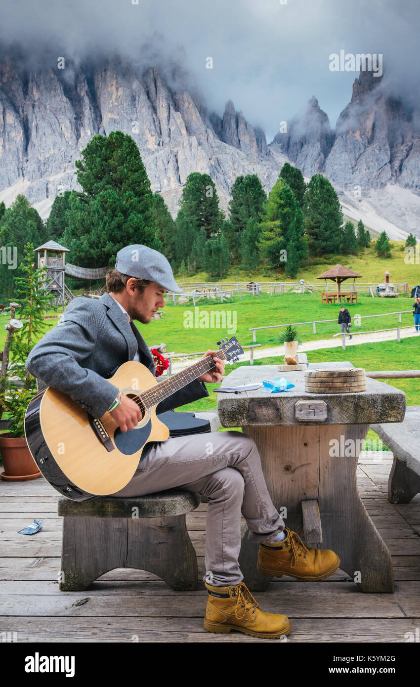 Junge gut gekleideten Mann (30-35) spielt eine Gitarre mit italienischen Dolomiten Felsformation Hintergrund Stockfoto
