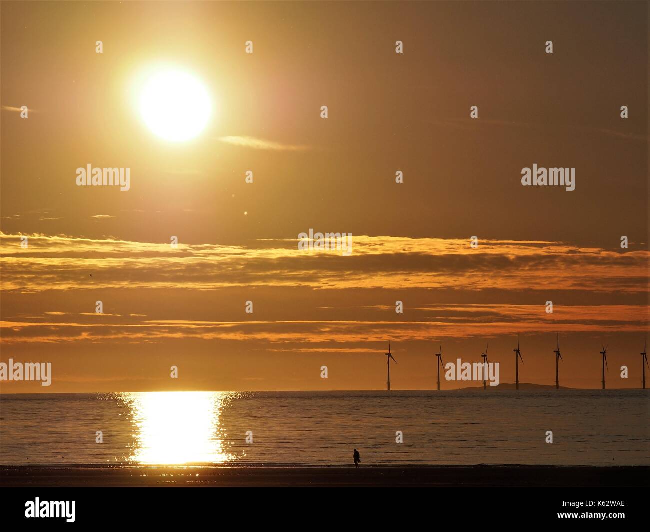 Walking am Strand, wenn die Sonne Mit "Robin Rigg Windfarm hinter, Maryport, Cumbria, Vereinigtes Königreich Stockfoto