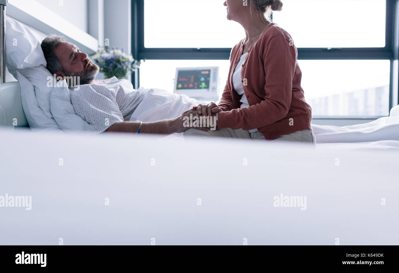 Warten auf Erholungskurs. Frau ihren Mann in die Krankenstation. Mann im Bett lag, mit Frau sitzt, indem Sie die Hand. Stockfoto