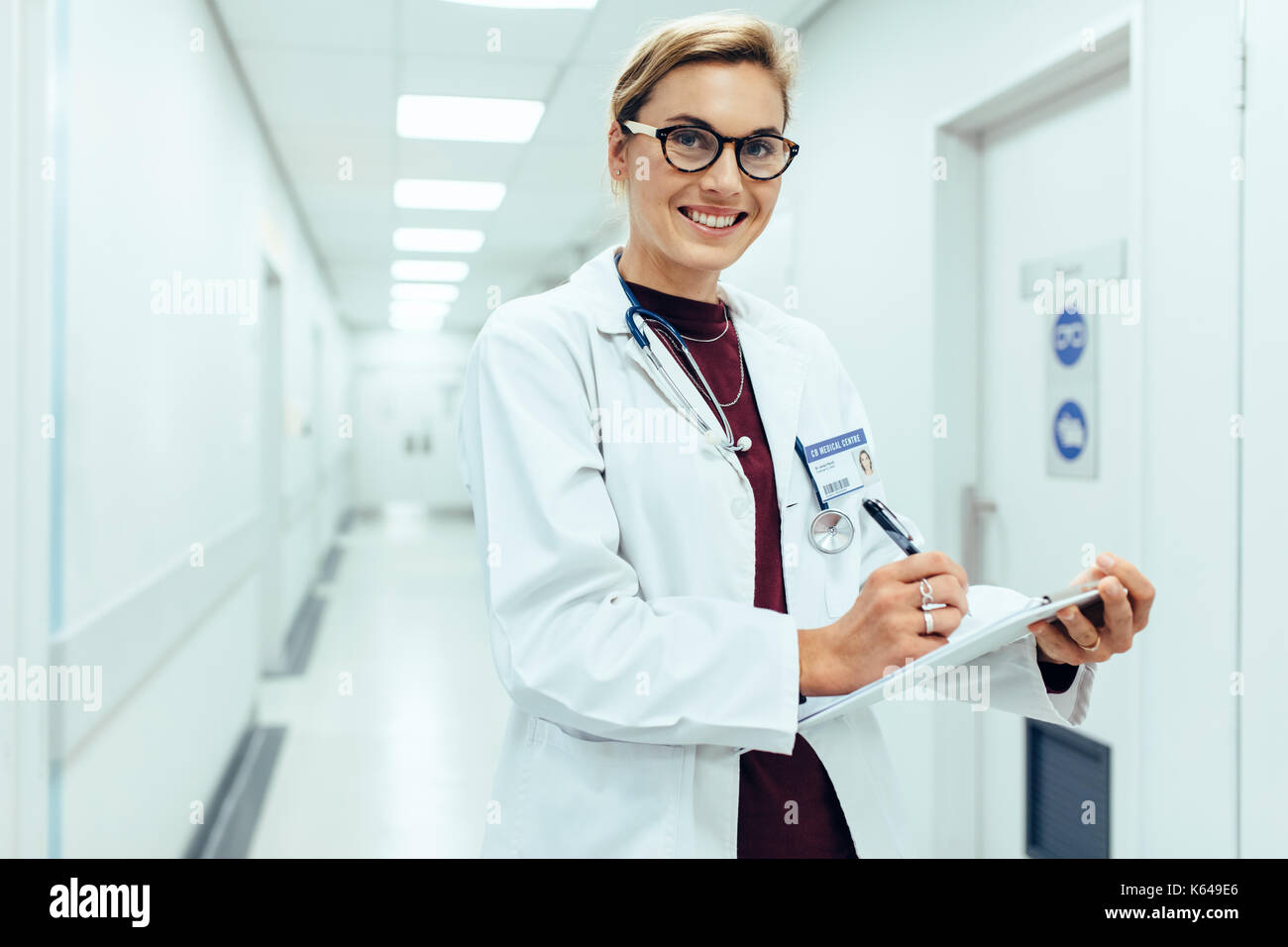 Portrait von lächelnden Frau Doktor im Krankenhaus Flur mit Zwischenablage. Kaukasische Medizin Praktiker schreiben medizinische Bericht und Ergebnisse Stockfoto