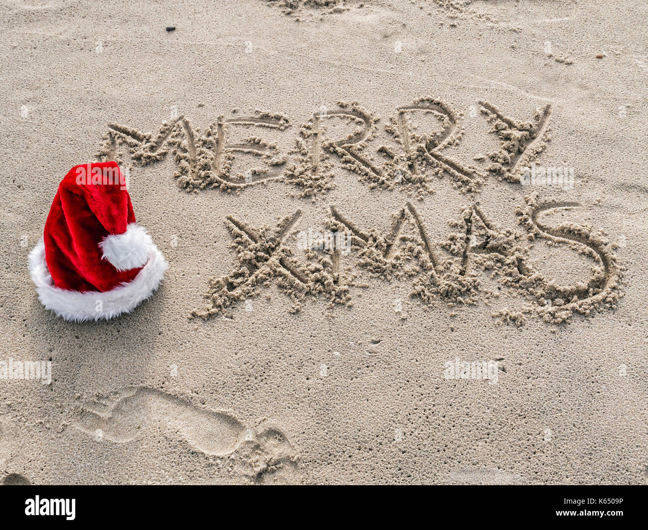 Merry Xmas grüße Hand - am Strand Sand mit roten Santa Claus hat geschrieben Stockfoto