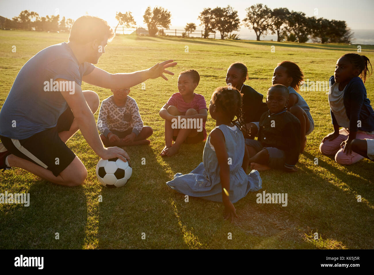 Grundschule Kinder und Lehrer sitzen mit Ball im Feld Stockfoto