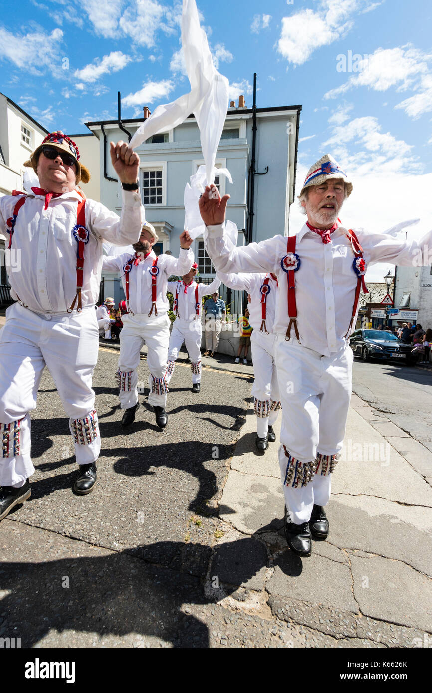 Tradition Morris Dancers, Hartley Morris Seite, stehend in 2 Zeilen in der Straße, winken weiße Taschentücher. Alle weiße Uniform mit roten Klammern und Strohhüte. Stockfoto