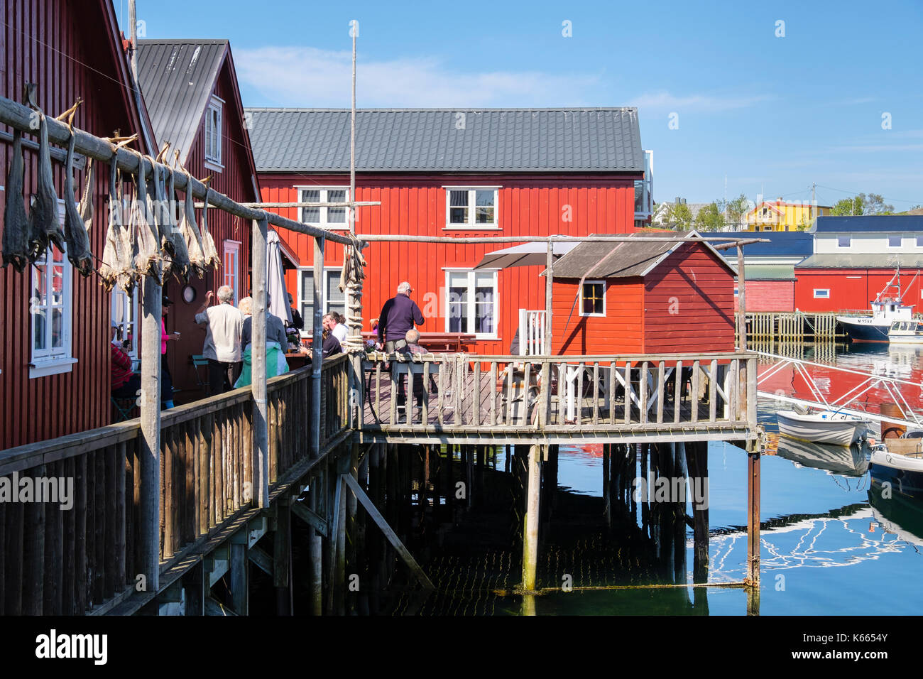 Touristen im Restaurant auf Stelzen in Kraemmervika Marina im Hafen im Sommer. Insel Vestvågøya Ballstad, Lofoten, Nordland, Norwegen Stockfoto