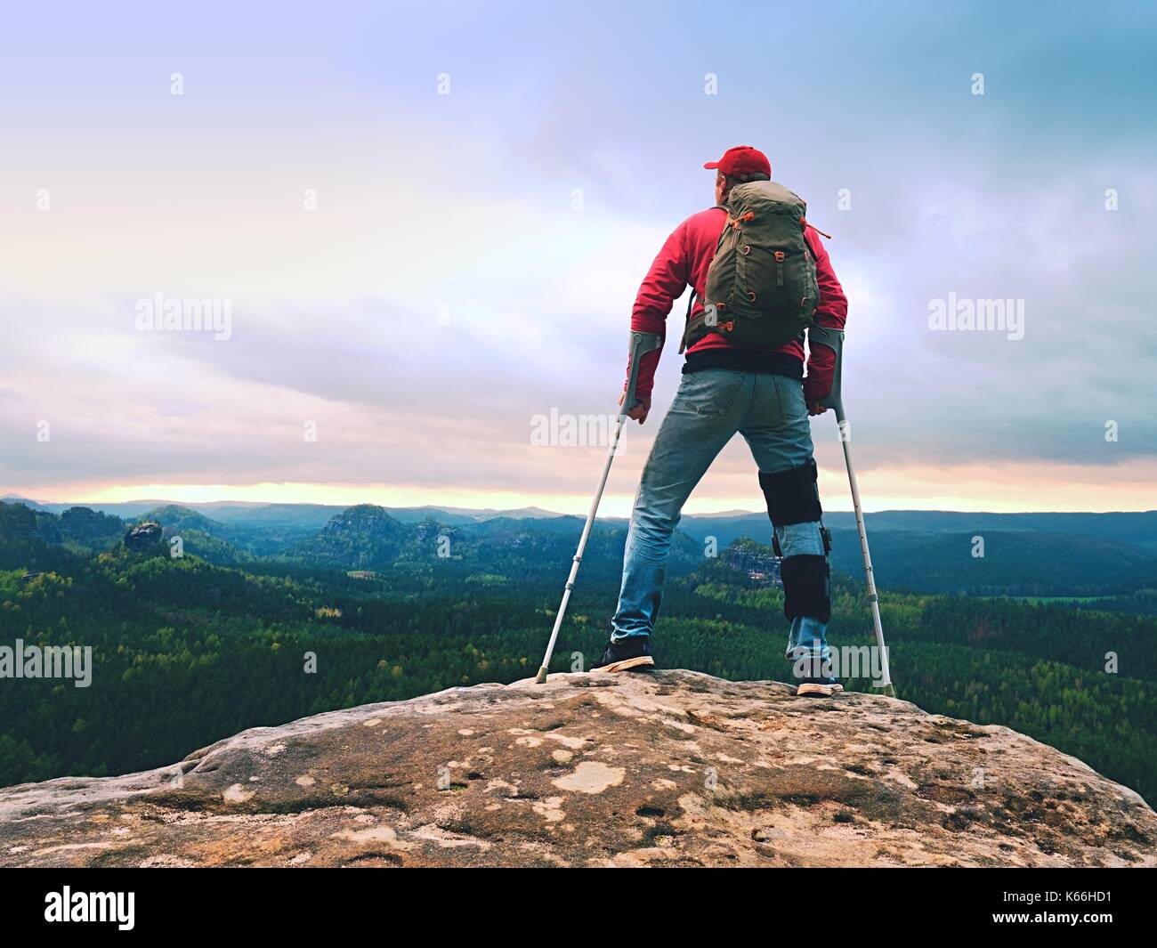 Behinderte Menschen mit Krücken steht auf einem großen Felsen und Blick in die Berge am Horizont. Wanderer Silhouette mit Medizin Krücke auf Berggipfel. Stockfoto