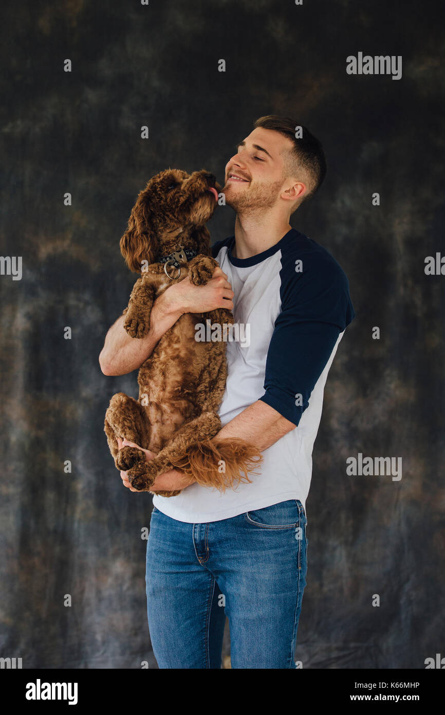 Mann mit seinem Hund in seine Arme. Sie sind gegen einen Studio Hintergrund und der Hund leckt das Gesicht des Mannes. Stockfoto