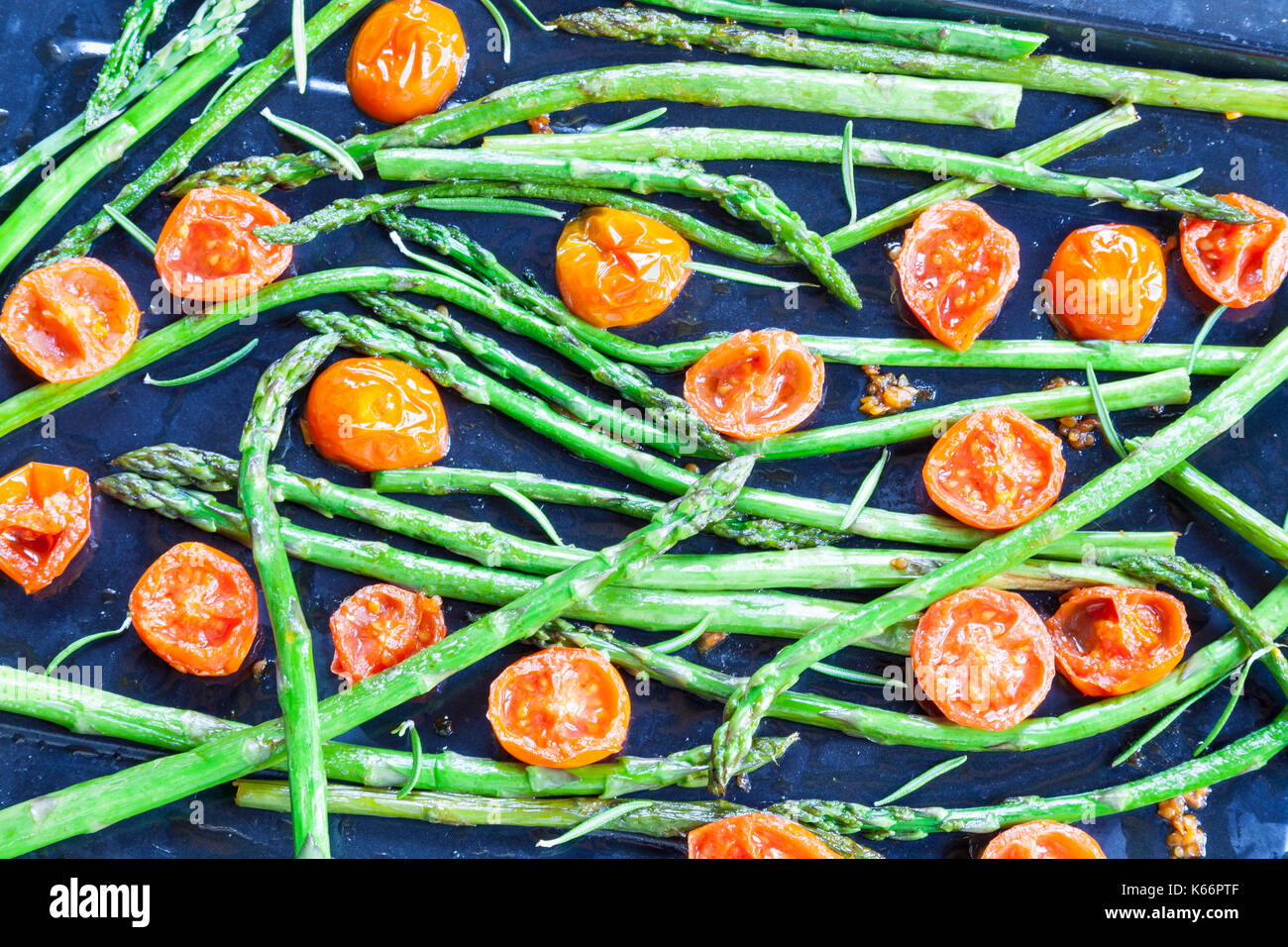 Gebratene frische Grüne Spargelspitzen und Cherry Tomaten gewürzt mit Rosmarin und Salz auf ein Backblech von oben gesehen für ein gourmet Vorspeise Stockfoto
