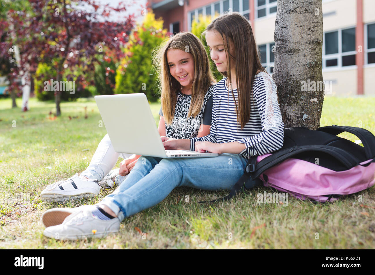 Zwei lächelnde Studentinnen sitzen auf dem Gras. Stockfoto