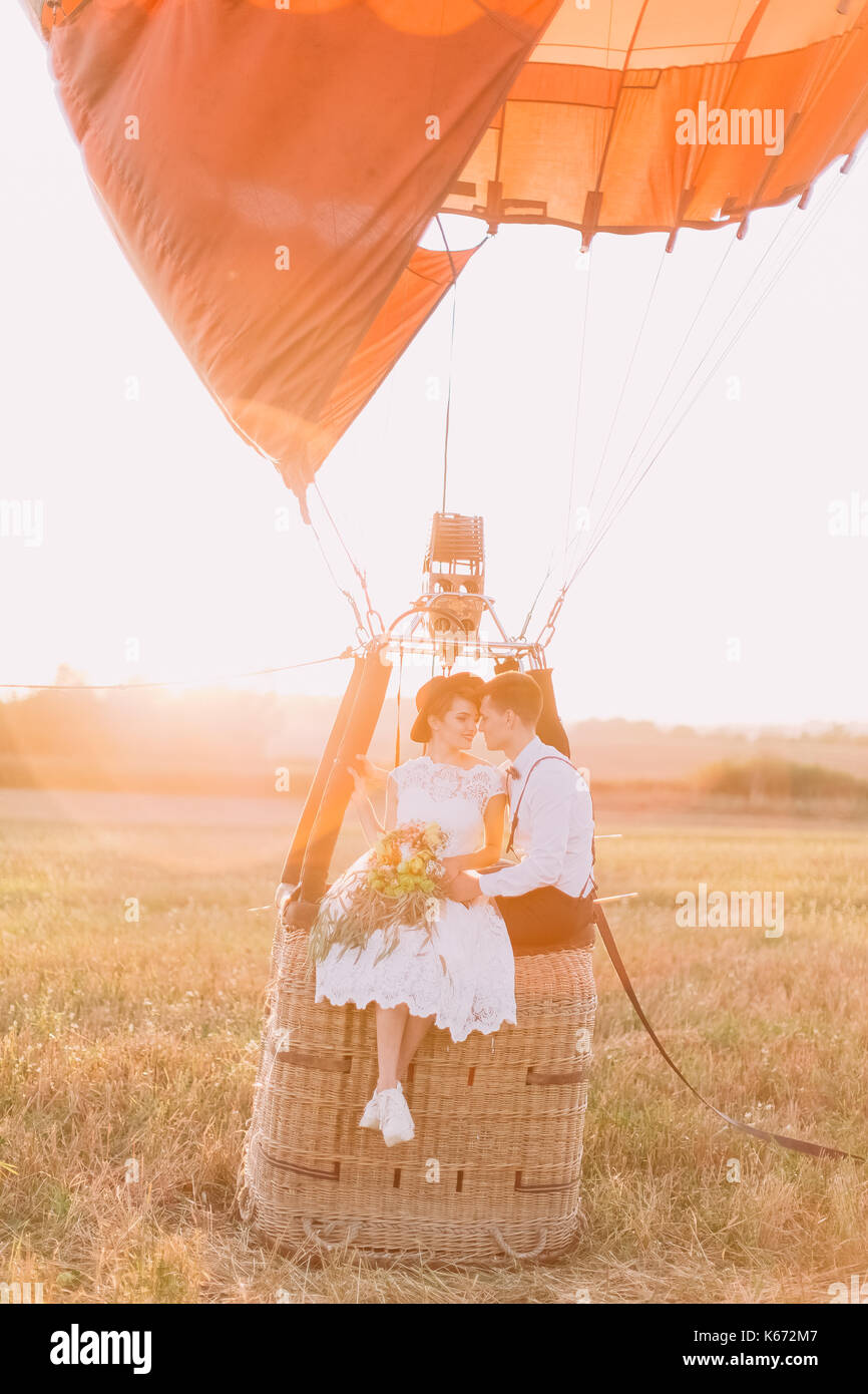 Die empfindlichen Augenkontakt betweet das glückliche Brautpaar sitzen auf dem airballoon Warenkorb in den sonnigen Tag im Feld. Stockfoto