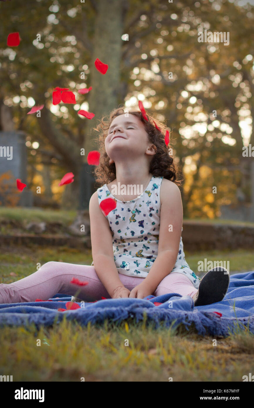 Kleines Mädchen mit dem Gesicht zur Sonne die Rosenblätter fallen auf Ihr Gesicht Stockfoto