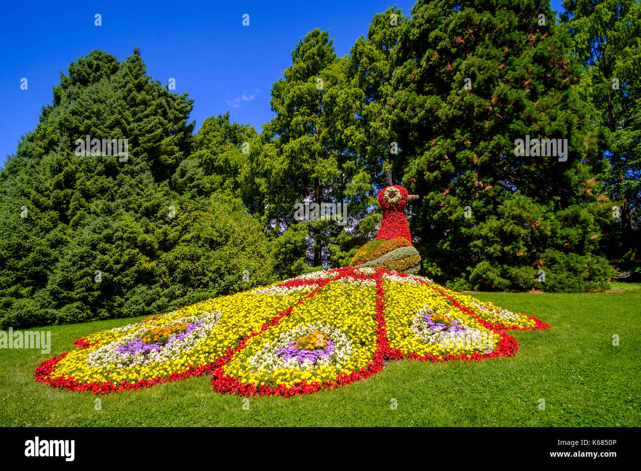 Eine bunte Statue eines Pfau wird durch Blumen Stockfoto