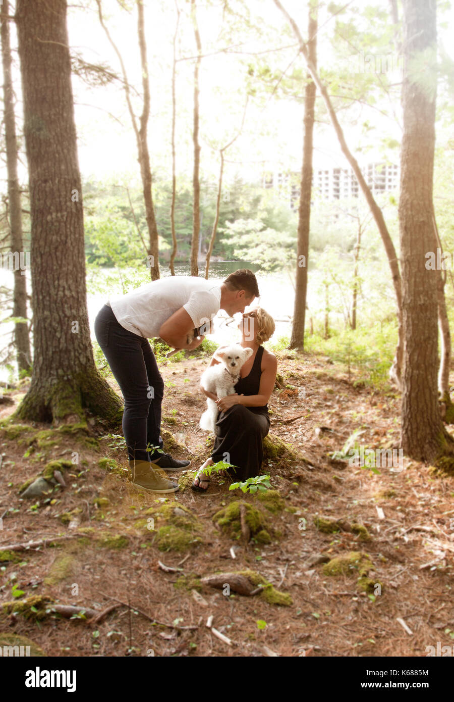 Ein weiches Sommer Glühen im Wald an einem See, wo ein Mann und eine Frau, die ihre Hunde und Kiss halten Stockfoto