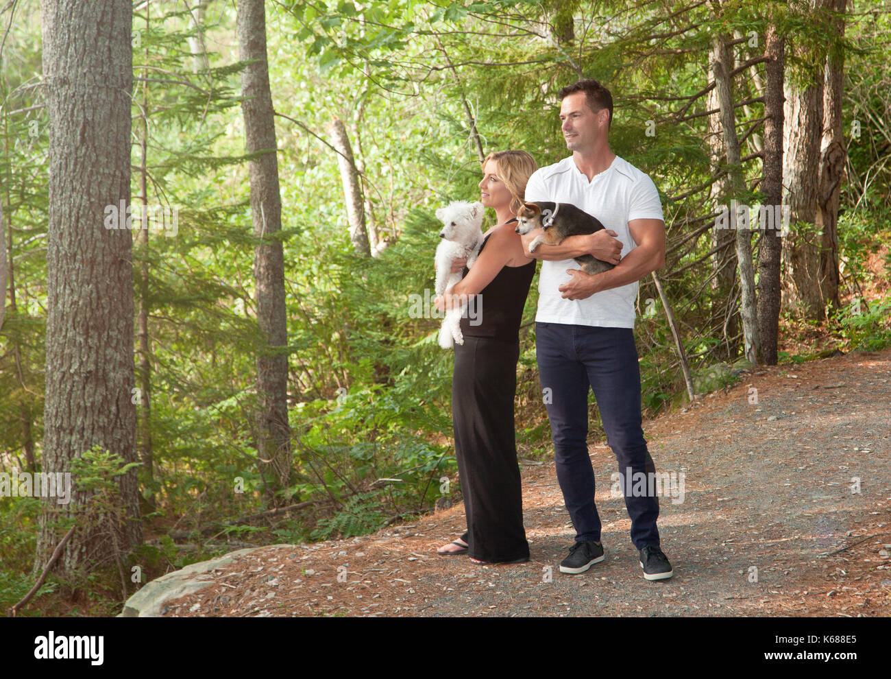 Ein Mann und eine Frau mit ihrem kleinen Hunde stehen auf einem Waldweg, mit Blick auf den Wald Stockfoto