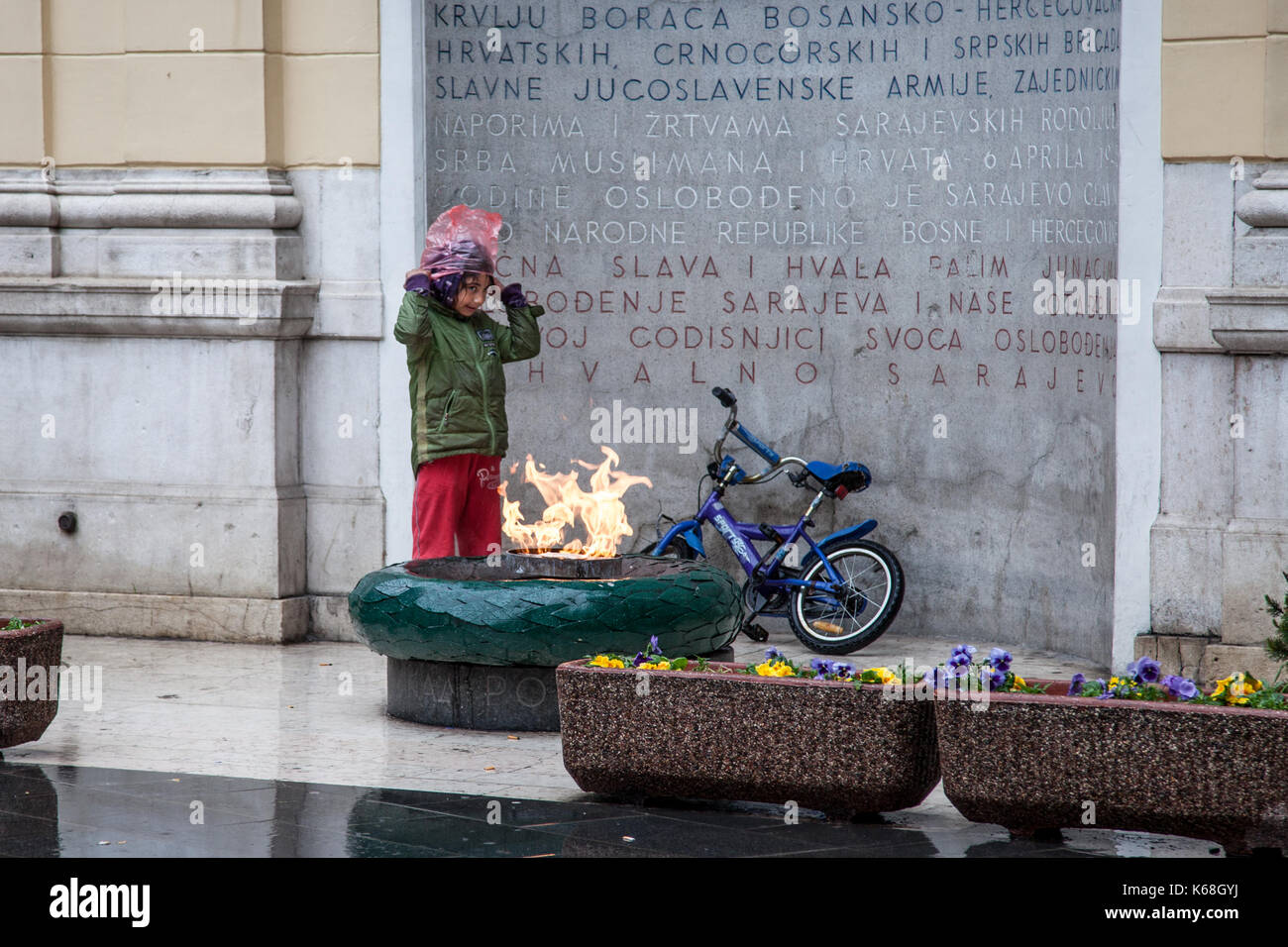 SARAJEVO, BOSNIEN UND HERZEGOWINA - 16. APRIL 2017: junge Roma-mädchen versucht, im Regen vor der ewigen Flamme ein WWII Monument in t zu warm Stockfoto