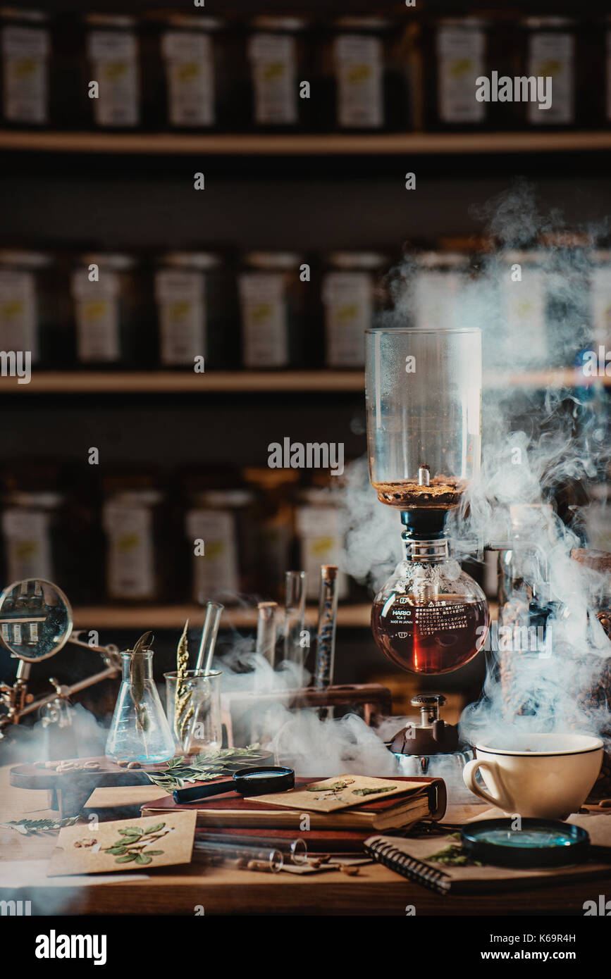 Die Zubereitung von Kaffee im Vakuum Kaffeemaschine mit aufsteigenden Dampf und einem Blumen still life. Alternative Kaffee brühen. Botaniker Arbeitsplatz. Professionelle b Stockfoto