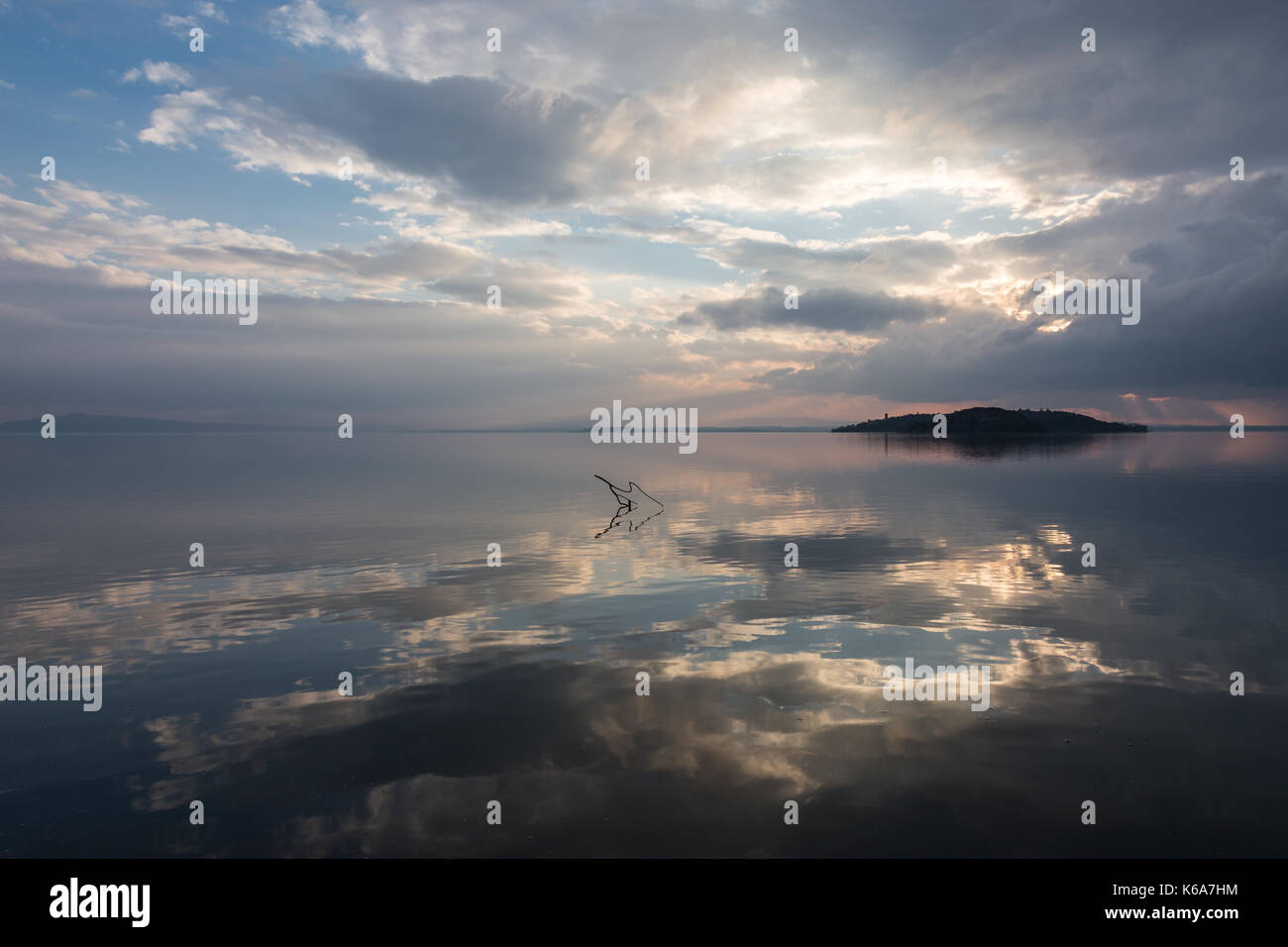 Perfekt symmetrische Reflexionen einer Insel und Wolken an einem See, mit warmen und weichen Sonnenuntergang Farben Stockfoto