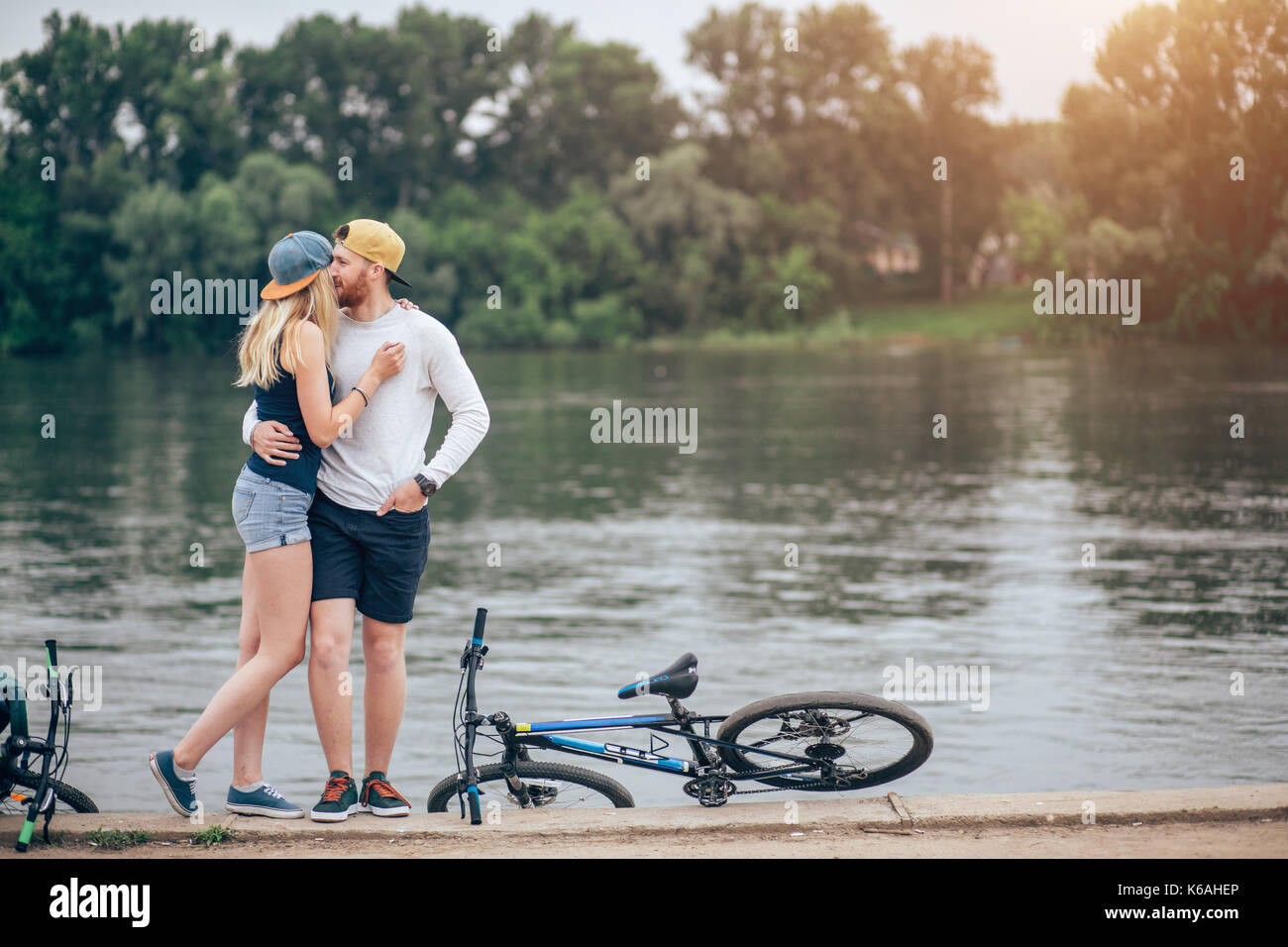 Romantisches Paar mit Fahrrädern Entspannen bei Sonnenuntergang am See. Verlieben Sie sich in das Konzept. Stockfoto Romantisches Paar mit Fahrrädern Entspannen bei Sonnenuntergang am See. Verlieben Sie sich in das Konzept. Stockfoto