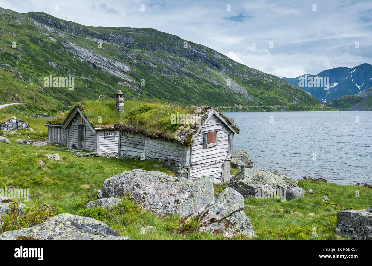 Alte märchenhafte Haus aus Holz mit Kamin aus gestapelten Schiefer und ein Dach mit Pflanzen und Bäume an einem Fjord in Norwegen mit Garten mit roten Blumen ein Stockfoto