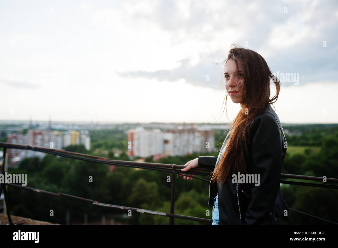 Portrait einer attraktiven jungen Frau in Schwarz Leder Jacke, Jeans und Turnschuhe stehen durch das Geländer auf dem Dach. Stockfoto