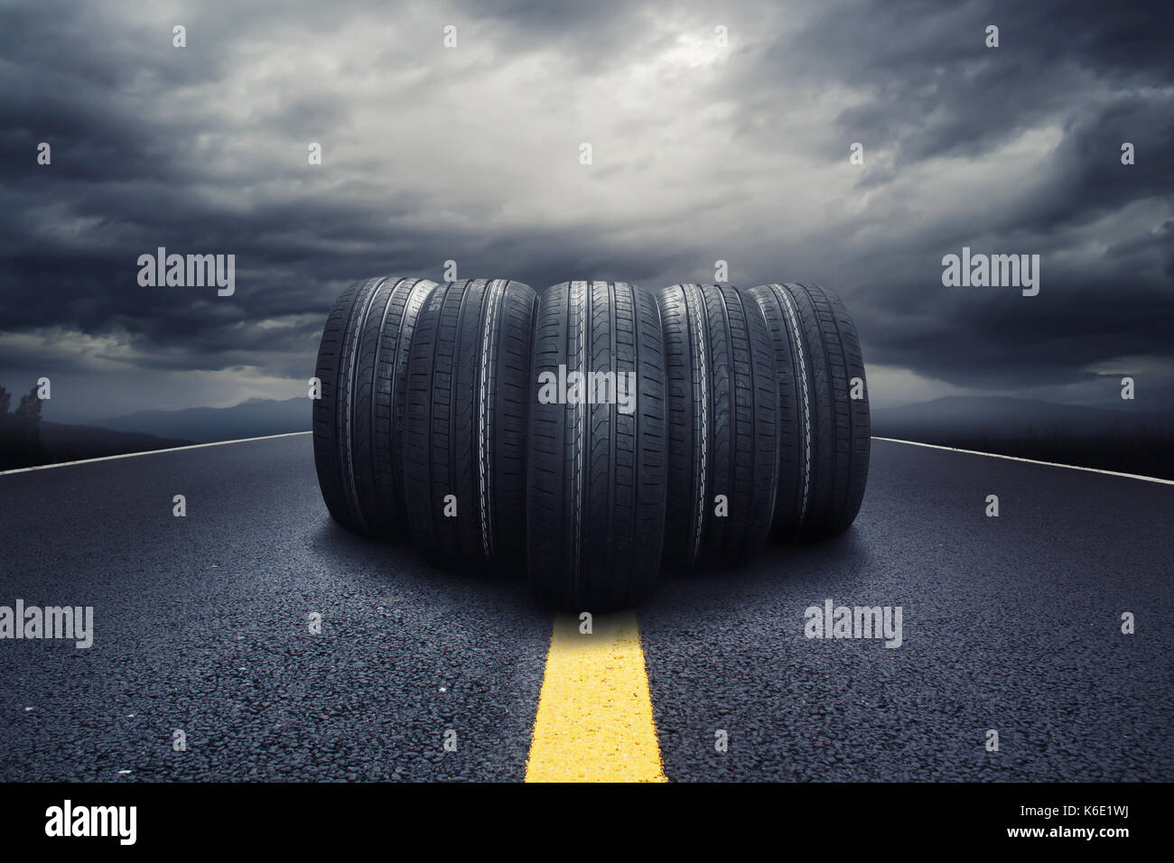 Fünf schwarze Reifen Rollen auf einer Straße mit Wolken Stockfoto