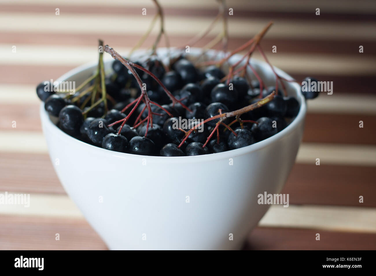Nahaufnahme des nassen Aronia Beeren in Weiß einfache Schüssel auf hölzernen Tisch Stockfoto
