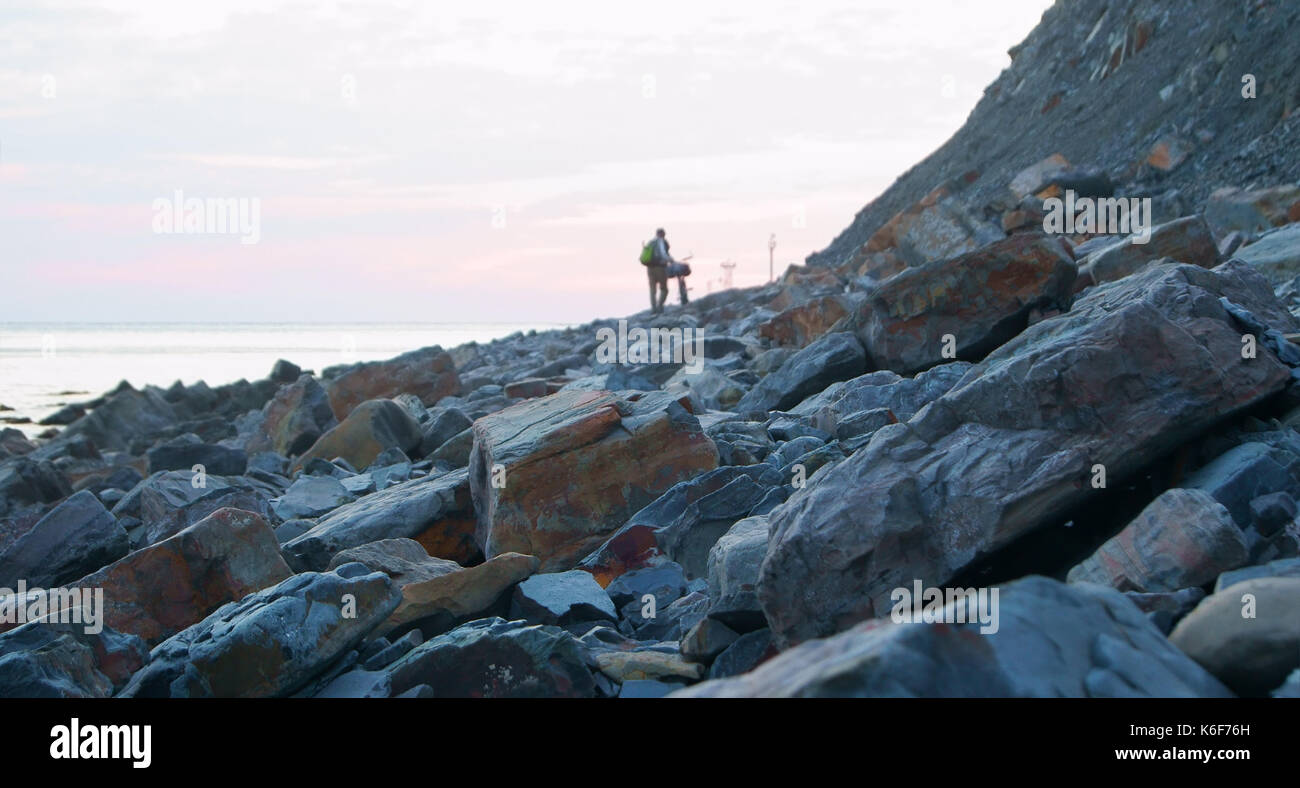Romantische Abend am Meer. Silhouette der unkenntlich Mann Weg entlang zu Fuß das Meer und die Berge mit dem Fahrrad in der Dämmerung. Stockfoto
