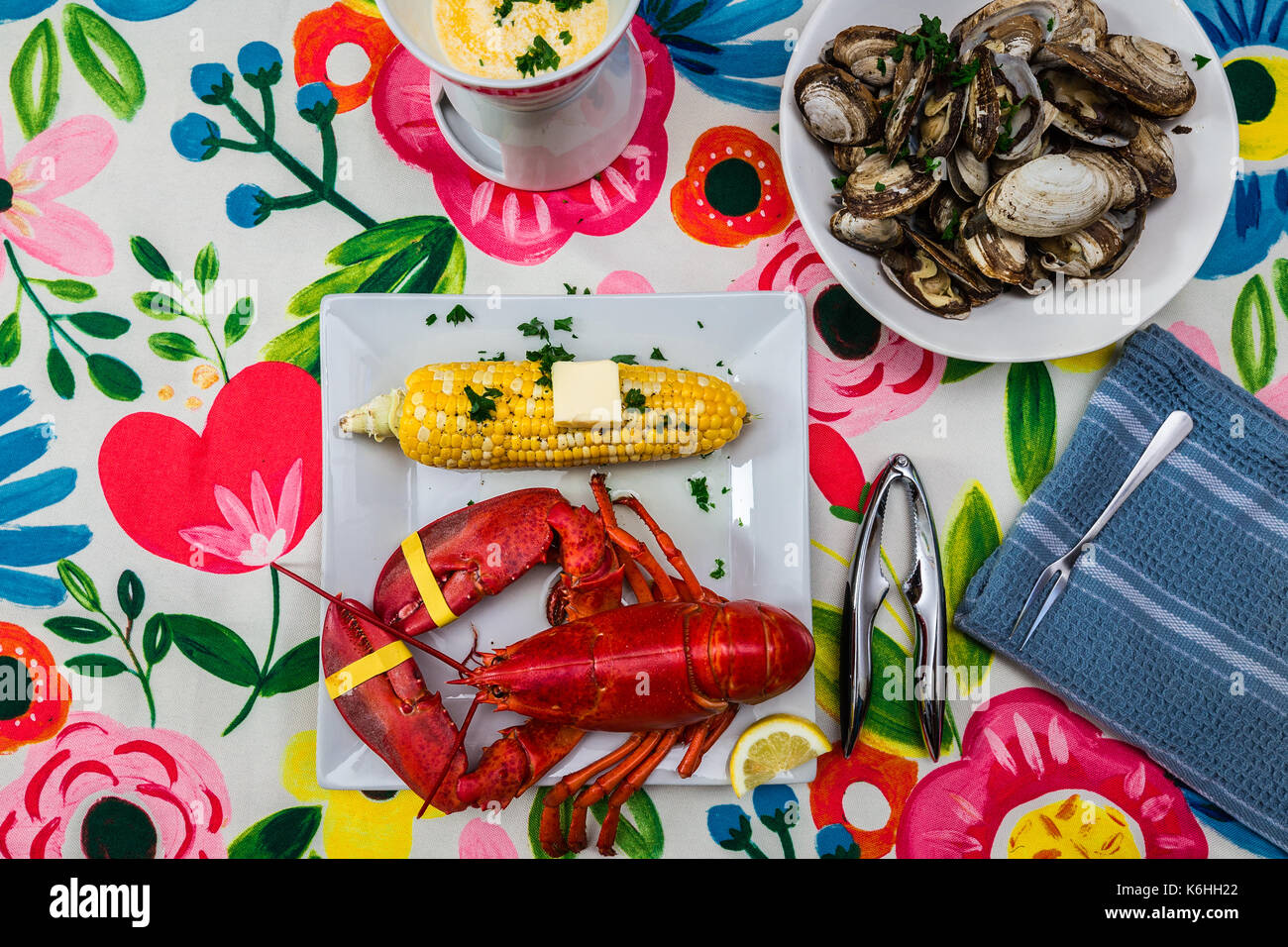 Hummer mit einer Schüssel mit Streamer Muscheln und Maiskolben. Eine Schale mit zerlassener Butter und eine Schale Cracker. Auf einem bunten Tischdecke Stockfoto