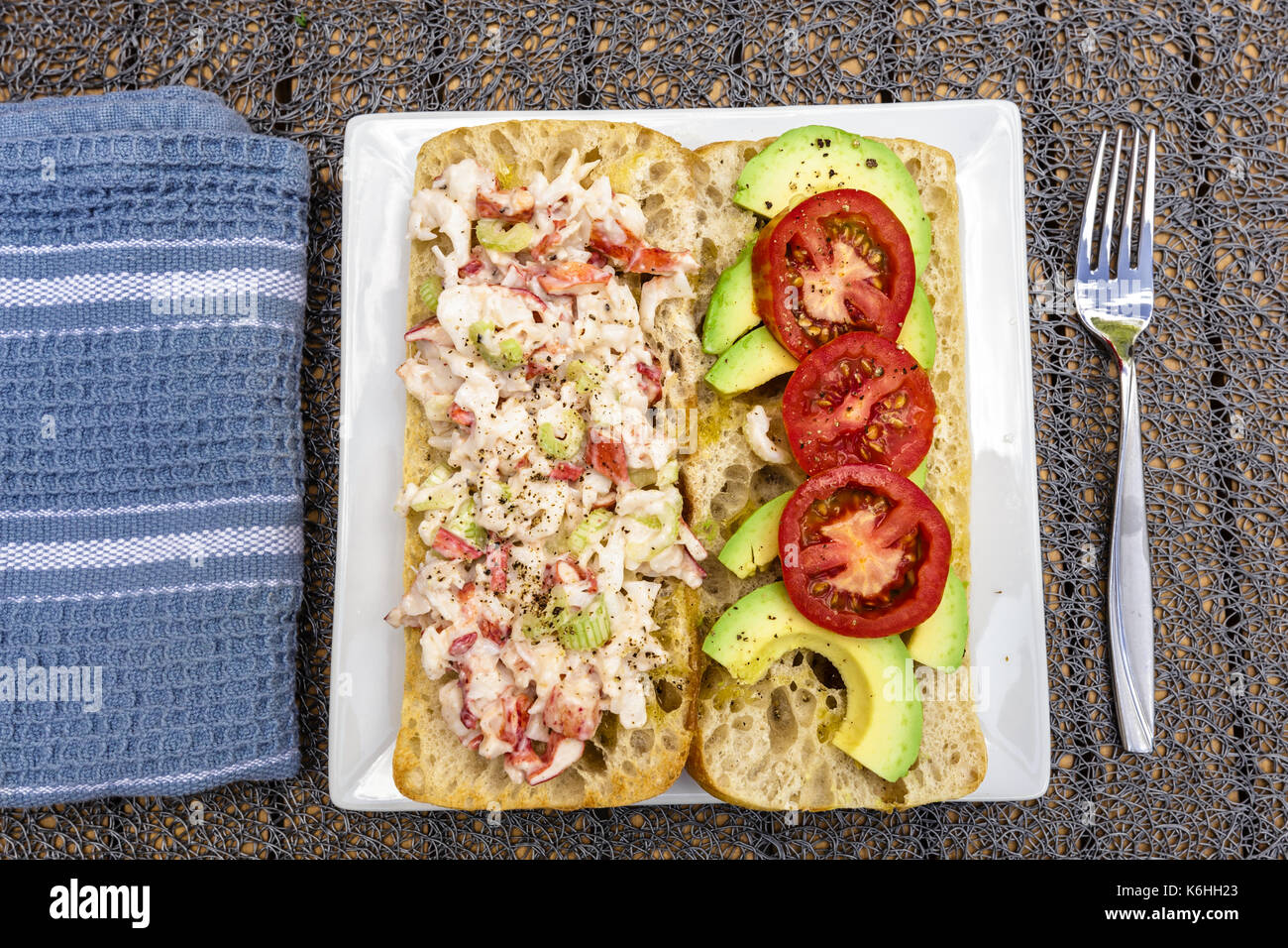 Im Sommer eine Auszeit von ein Lobster Roll. Mit Hummer Fleisch gemacht, ein wenig Mayo, in Scheiben geschnittenen Avocado und in Scheiben geschnittenen Tomaten. Auf ein Ciabatta Roll auf einem weißen serviert. Stockfoto