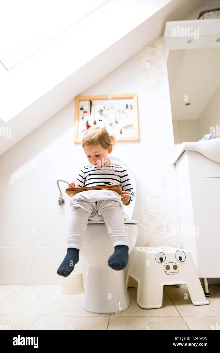 Kleines Mädchen mit Tablet auf der Toilette sitzen. Stockfoto