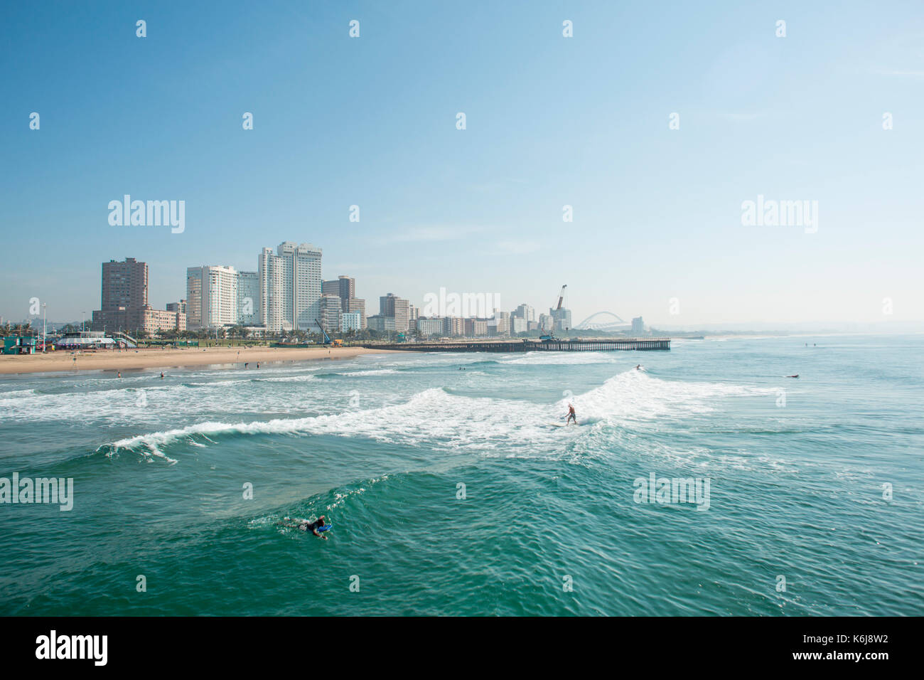 Surfer reiten Wellen in der Nähe von Pier auf der Golden Mile mit Skyline von Durban, Südafrika Stockfoto