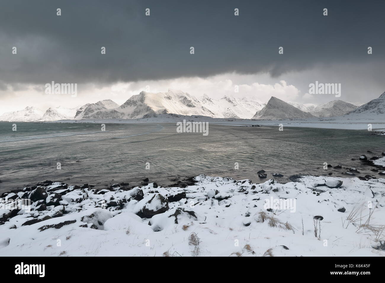 SEwards - Schnee Ytresand Strand - Sandbotnen Bucht - stürmischen Himmel. - Bora-Nesfjellet Volandstinden-Sautinden - Nonstinden-Stortinden - Flakstadtinden montieren Stockfoto